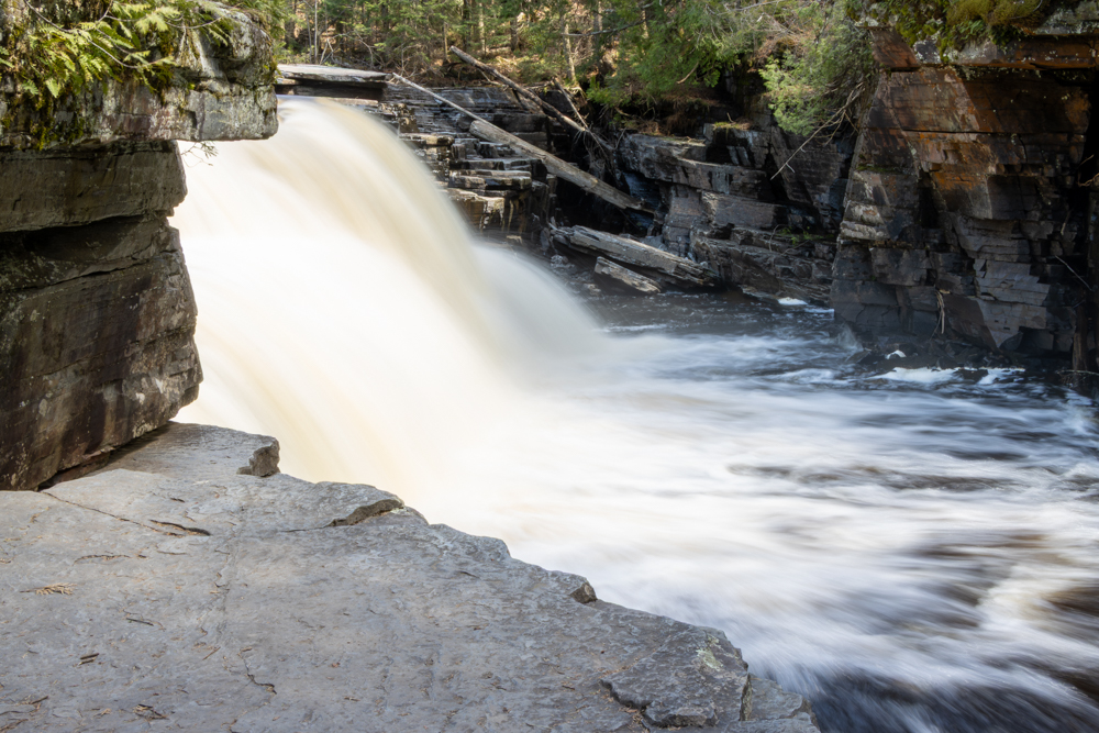 Long-exposure photograph of Canyon Falls on the Sturgeon River, cream-colored water plunging into a dark basalt gorge, photographed by Forbes Robertson in Baraga County, Michigan.